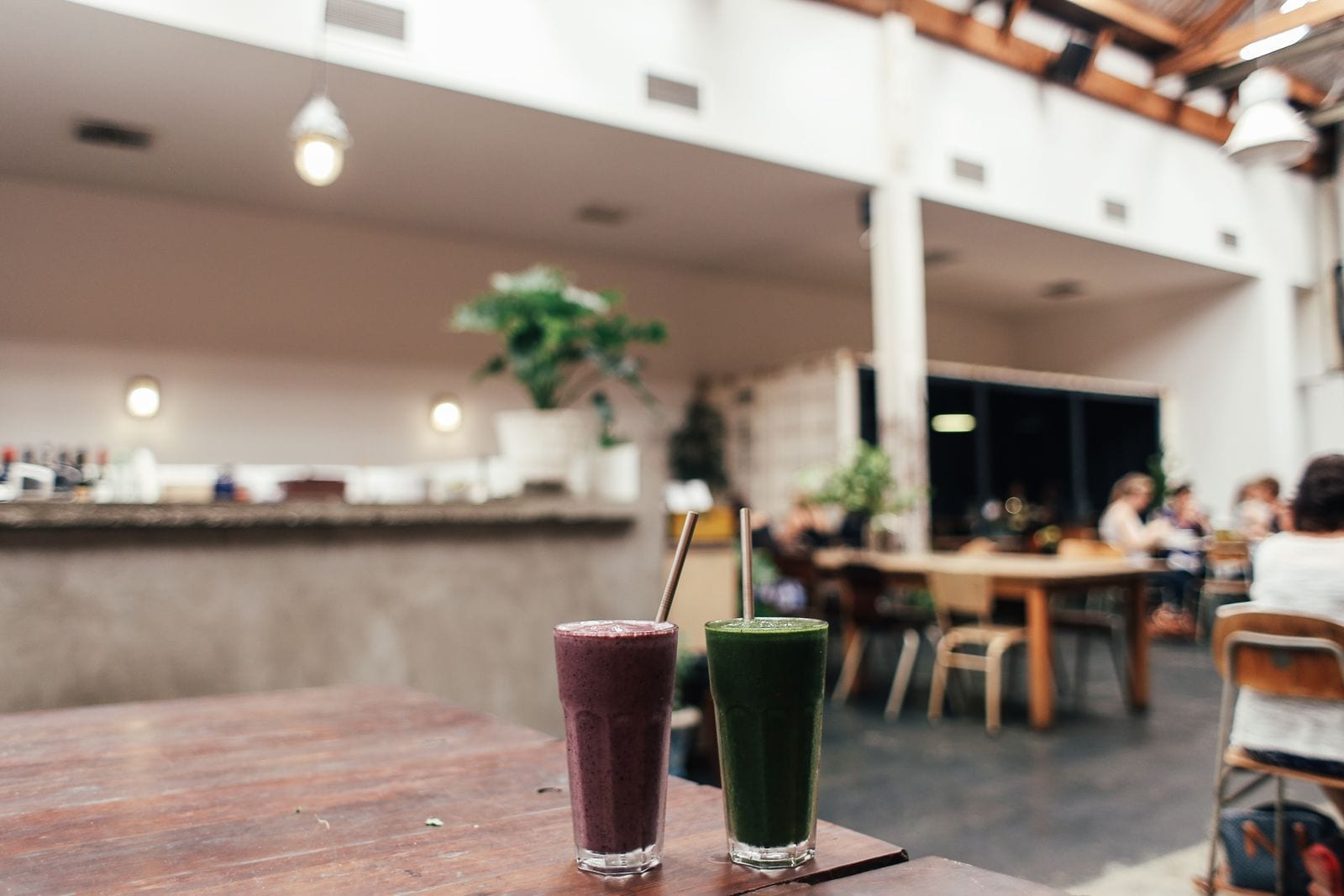 Two finished smoothies on a wooden cafe table with a counter and seating area in the background