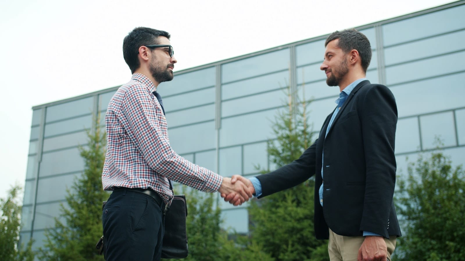 Two businessmen shaking hands outside a modern office building
