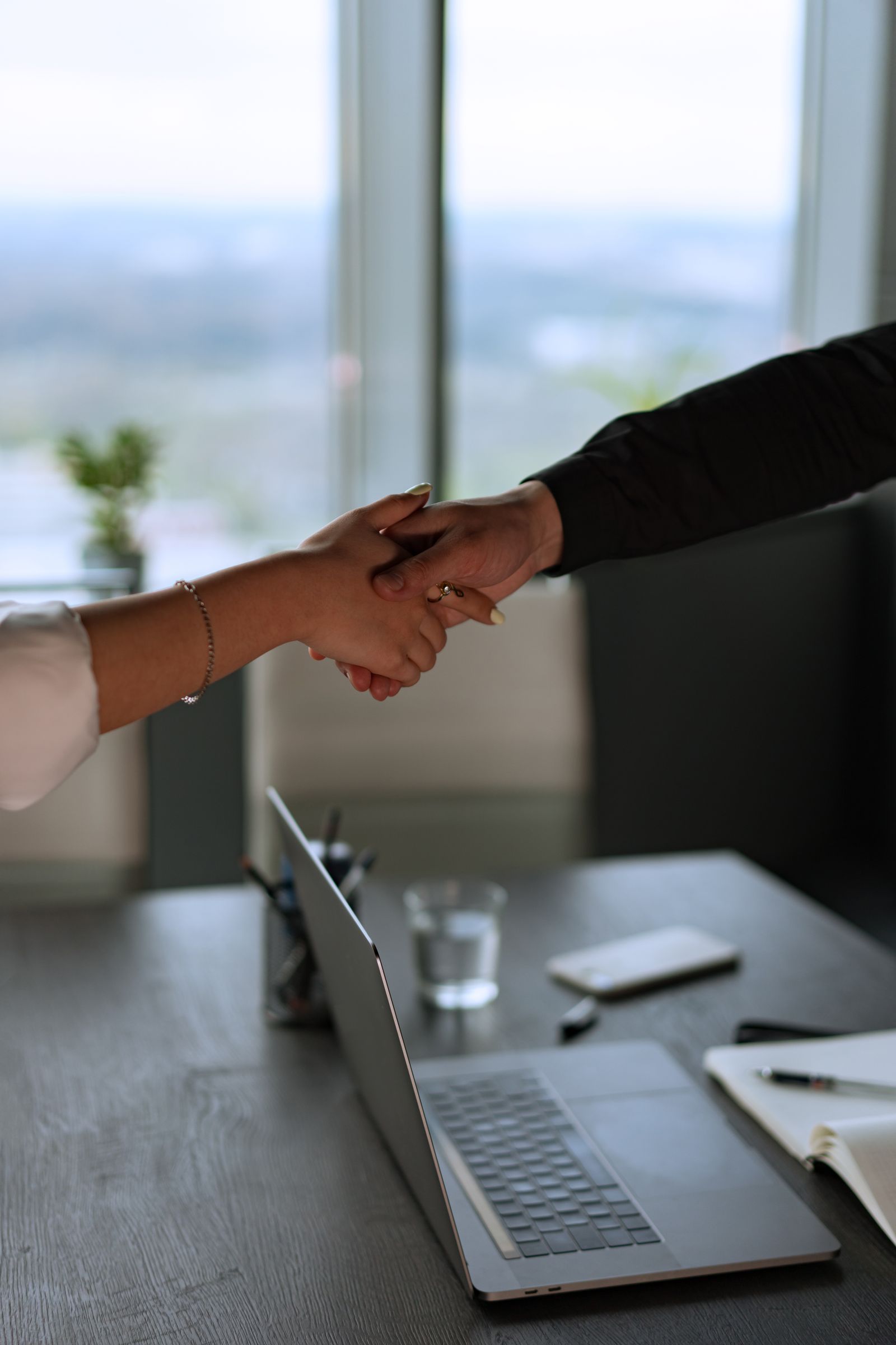 Two people shaking hands to close a deal across an office desk with a laptop