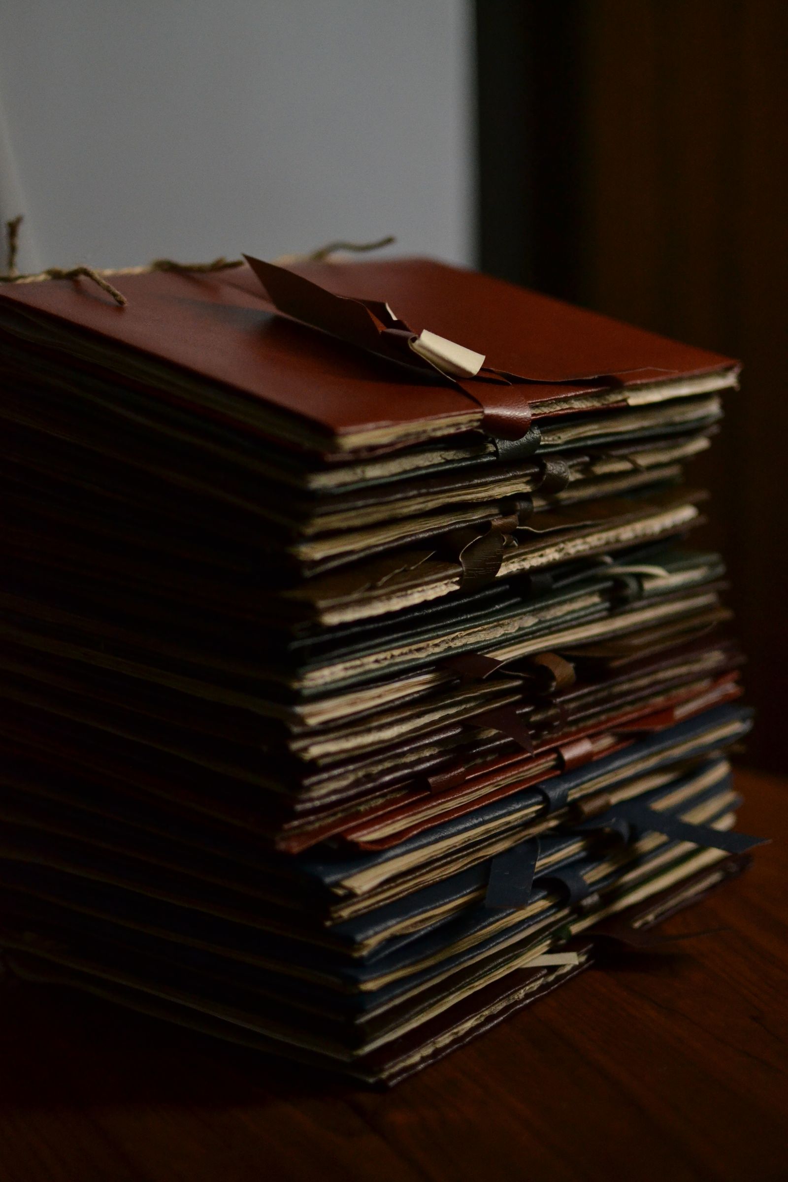 A tall stack of leather-bound ledgers and folders tied shut on a desk