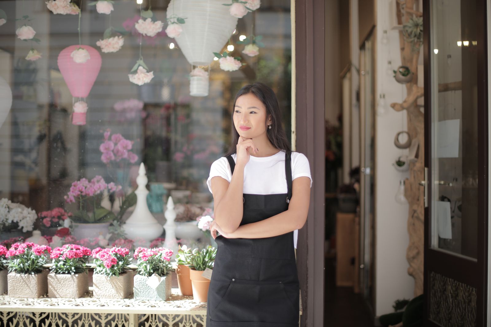 A shop owner in an apron standing in the doorway of her flower shop