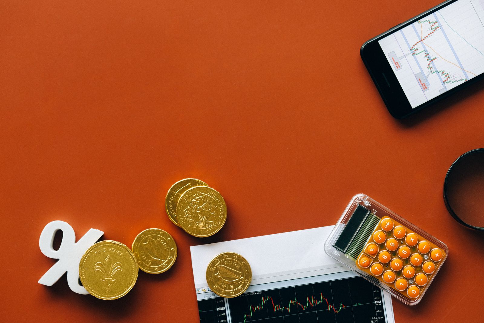 A percent symbol beside stacks of gold coins and a phone showing a chart