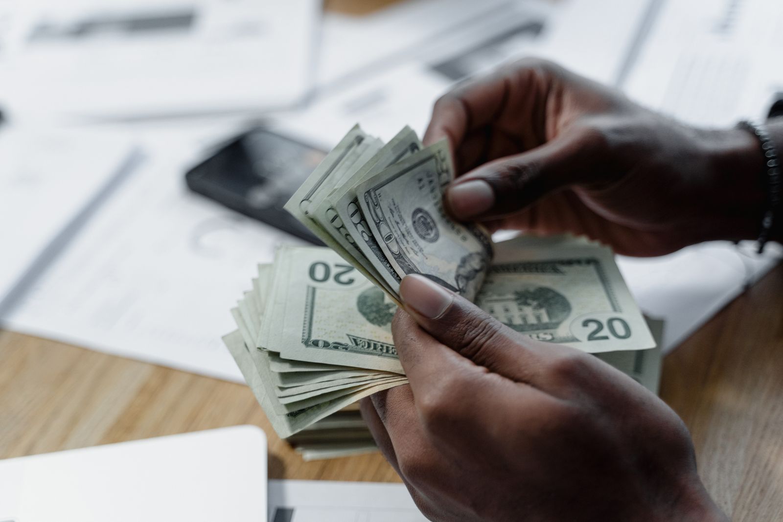 Hands counting a small stack of twenty-dollar bills over documents