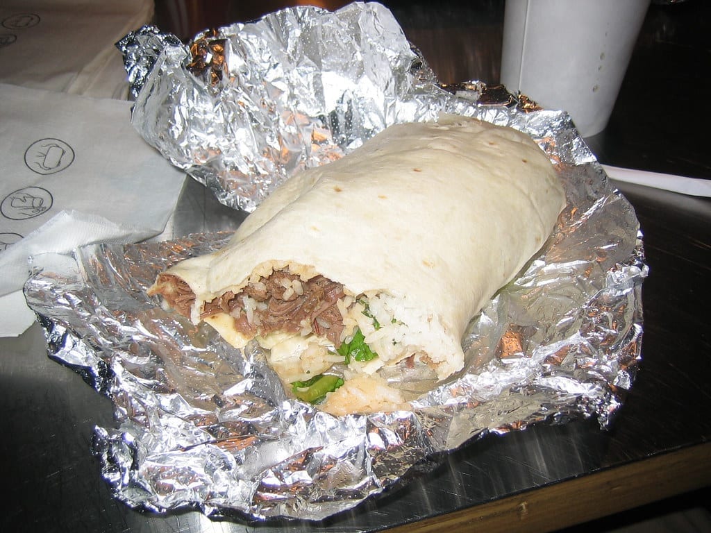A Chipotle burrito unwrapped in foil on a branded napkin, showing rice, meat, and greens