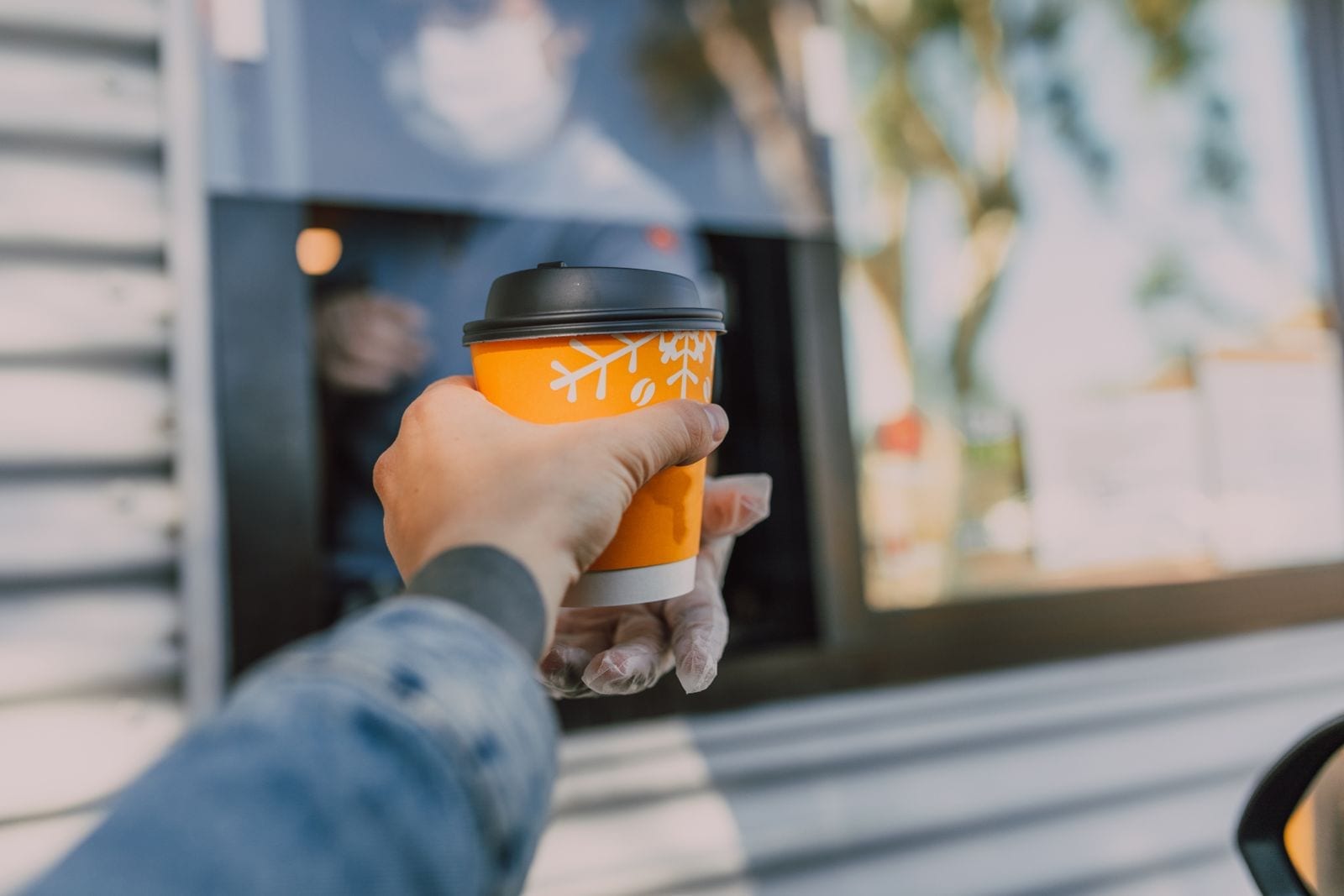 A hand reaching out to receive a hot drink through a drive-thru coffee window