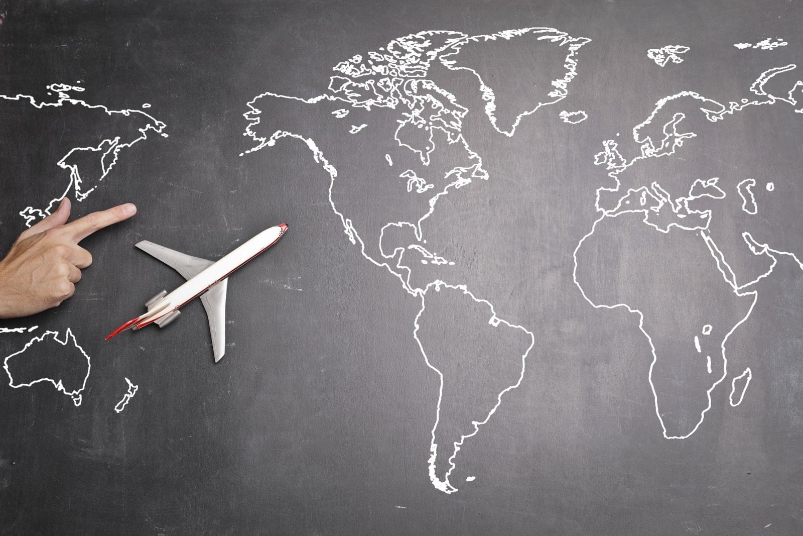 A hand pointing at a chalkboard-style world map next to a toy airplane