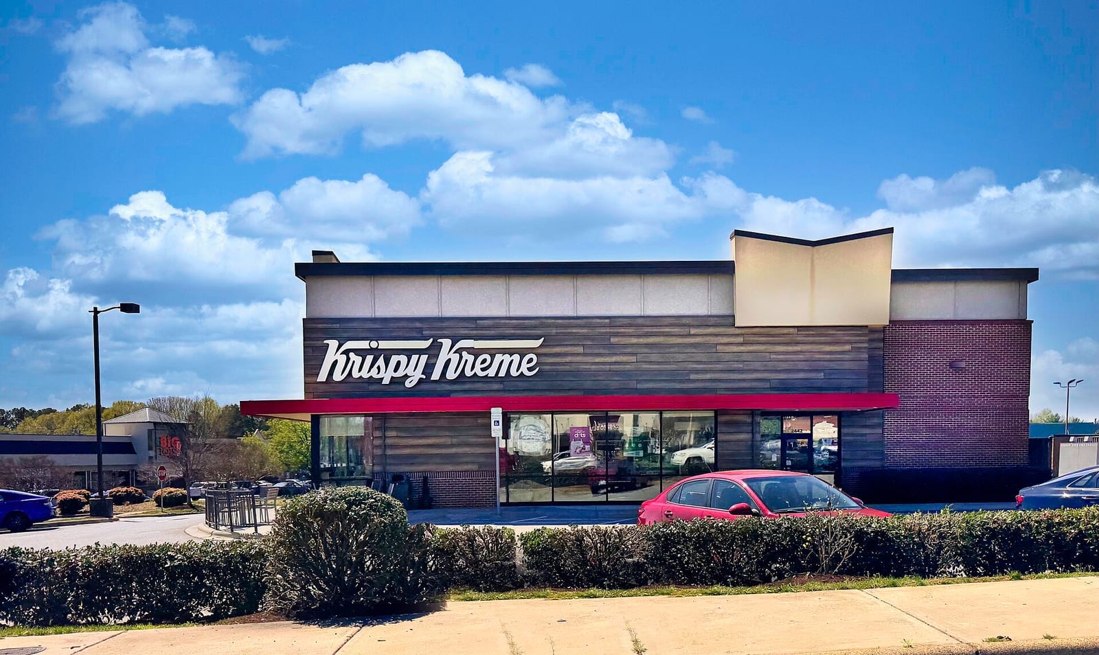 Modern Krispy Kreme storefront with red-and-white script signage and a red canopy above the entrance