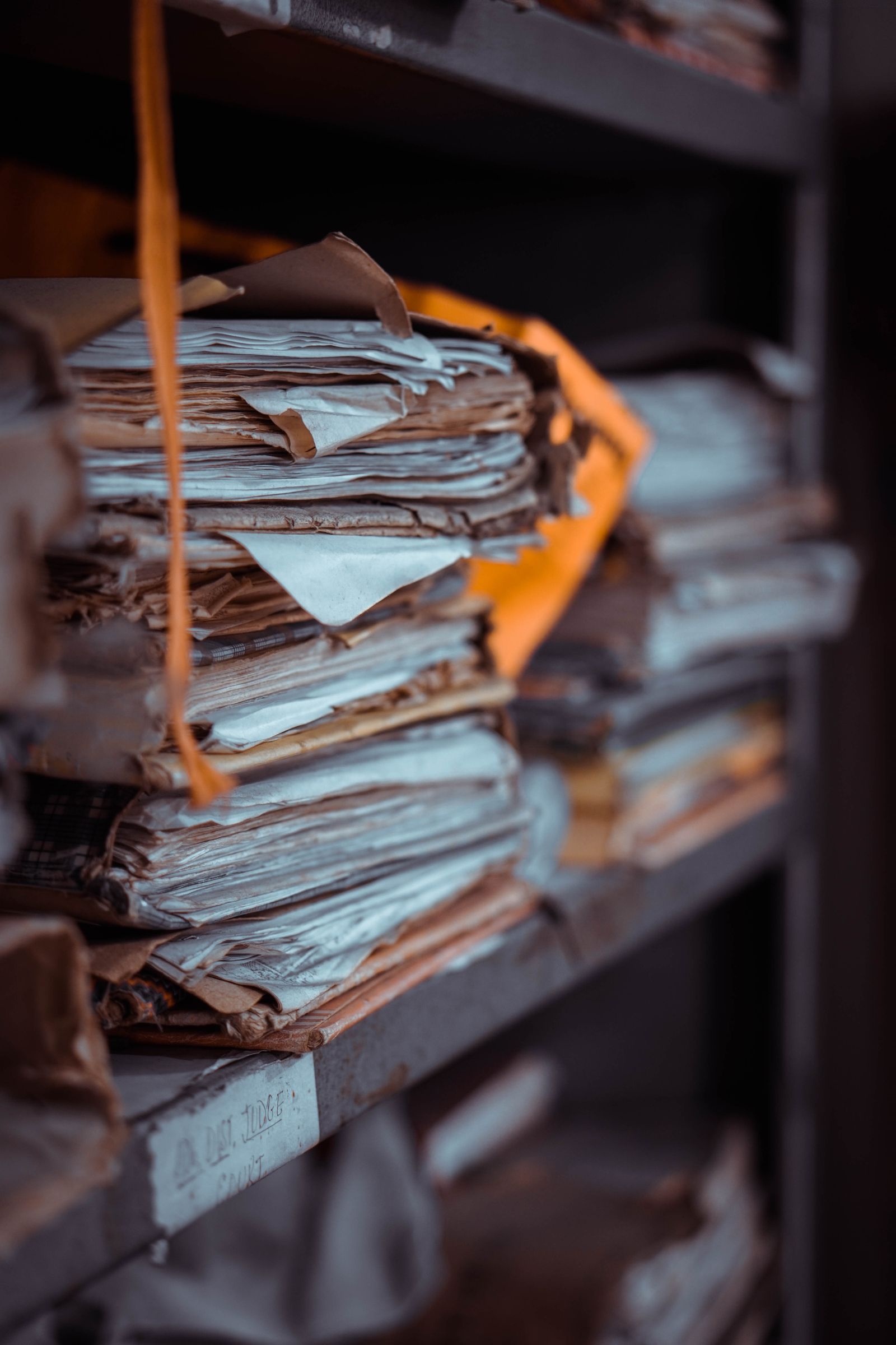 Bundles of paper case files tied with string, stacked on the metal shelves of a records archive