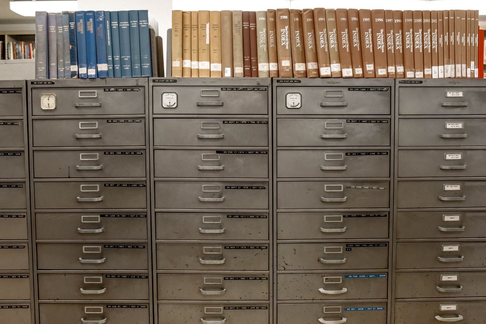 Bound annual index volumes shelved in a row above grey filing cabinets whose drawers are labelled with date ranges
