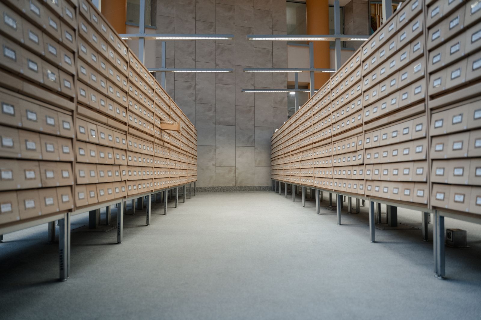 Two long rows of small wooden archive drawers receding toward the back wall of a quiet, empty records room